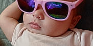 Skye is registered to the contest to win money with this photo: baby, child, sunglasses, pink, reflection, face, feet, clothing, lying_down, relaxed, indoor, cute, fashion, person, infant, portrait, soft_texture, blanket, casual, resting