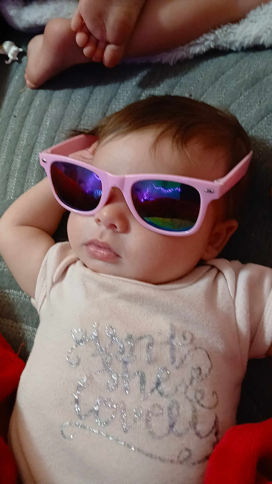 Skye is registered to the contest to win money with this photo: baby, child, sunglasses, pink, reflection, face, feet, clothing, lying_down, relaxed, indoor, cute, fashion, person, infant, portrait, soft_texture, blanket, casual, resting