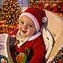 baby, celebration, child, christmas, christmas_tree, cozy, cute, decorations, festive, happy, high_chair, holiday, indoor, infant, lights, red_clothing, santa_hat, seasonal, smiling, toy