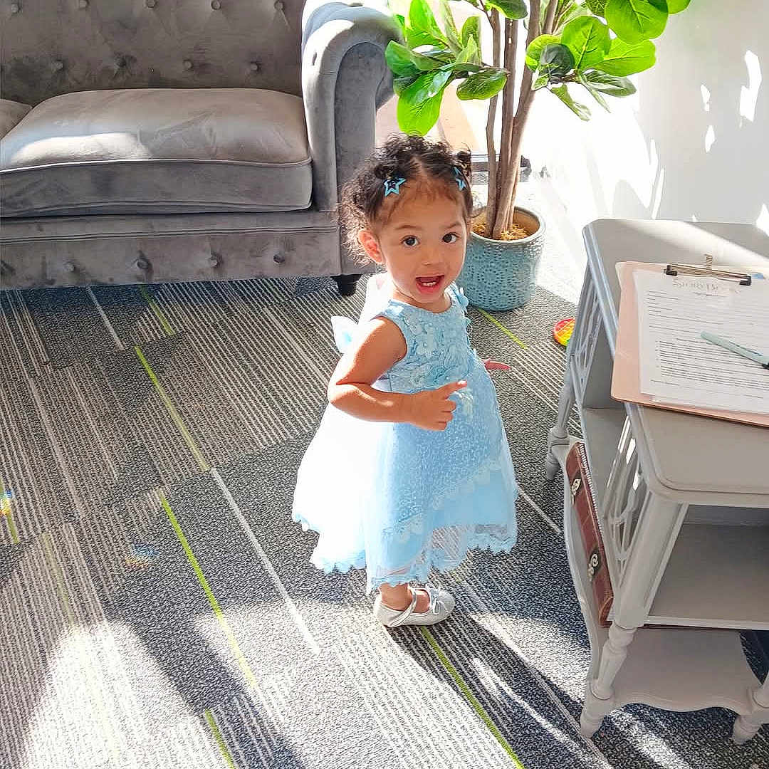 Lilyanna is registered to the contest to win money with this photo: architecture, building, child, clothing, couch, dress, face, female, furniture, girl, head, homedecor, indoors, livingroom, person, photography, plant, portrait, pottedplant, sitting