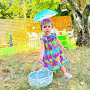 Mila participe au concours pour gagner de l'argent avec cette photo : backyard, basket, child, colorful, curious, dress, fence, footwear, grass, headband, nature, outdoor, plastic_chair, slide, standing, sunny, toddler, toy, tree, umbrella