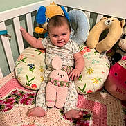 Addilynn is registered to the contest to win money with this photo: baby, crib, plush_toy, cushion, crocheted_bunny, blanket, child, smiling, indoor, person, cute, toy, colorful, soft, decor, happy, seated, head, foot, pajamas