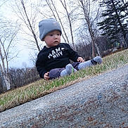 Jonathan is registered to the contest to win money with this photo: toddler, child, grass, beanie, socks, concrete, outdoor, trees, winter, curious, clothing, nature, sitting, side_view, young_child, casual, daylight, park, bare_trees, cold_weather