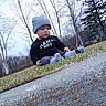 toddler, child, grass, beanie, socks, concrete, outdoor, trees, winter, curious, clothing, nature, sitting, side_view, young_child, casual, daylight, park, bare_trees, cold_weather