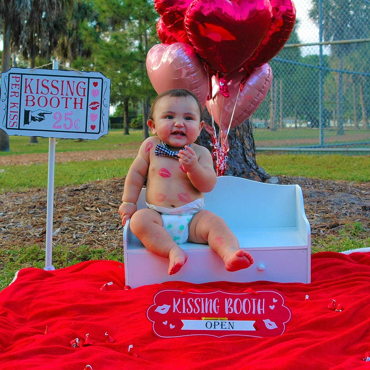 Joel joined the competition — help win amazing prizes! baby, balloons, bench, bow_tie, candy, child, cute, daylight, diaper, grass, happy, heart_shape, kissing_booth, outdoor, park, playful, red_blanket, sign, smiling, tree