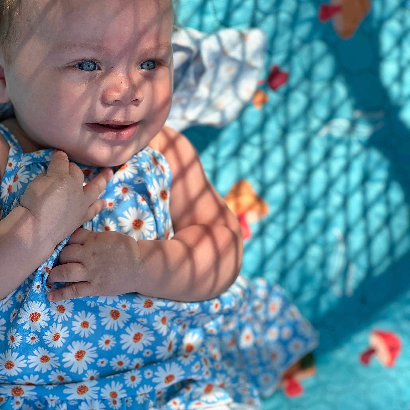 Malilah is registered to the contest to win money with this photo: baby, child, blue_eyes, floral_dress, sunlight, shadow_pattern, blanket, turquoise, cute, smiling, hand, skin, portrait, infant, outdoor, playful, colorful, happy, young_child, person
