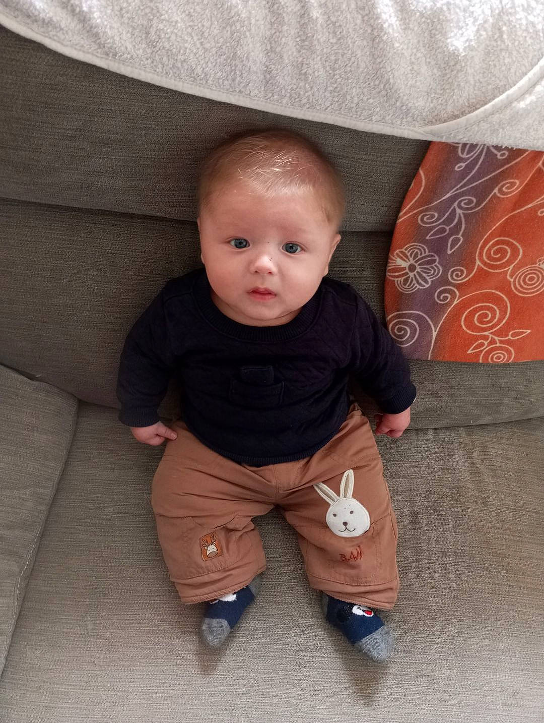 Tiago a rejoint le concours — aidez-le/la à gagner de superbes lots ! baby, baby_toddler_clothing, beige, cheek, comfort, couch, eye, finger, flooring, foot, human_leg, leg, linens, person, sitting, skin, sleeve, sock, textile, toddler