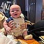 baby, smile, overalls, striped_shirt, hands, nail_polish, table, food, knife, indoor, wooden_furniture, high_chair, person, face, child, happy, cute, seated, cozy, restaurant