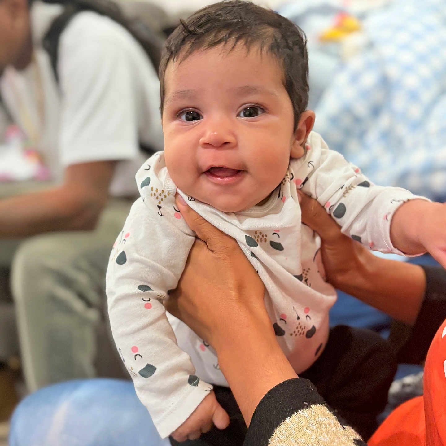 Twyla is registered to the contest to win money with this photo: baby, blurred_background, child, closeup, clothing, cushion, cute, eyes, face, hands, happy, holding, indoor, infant, patterned_outfit, person, portrait, seated_person, skin, smiling