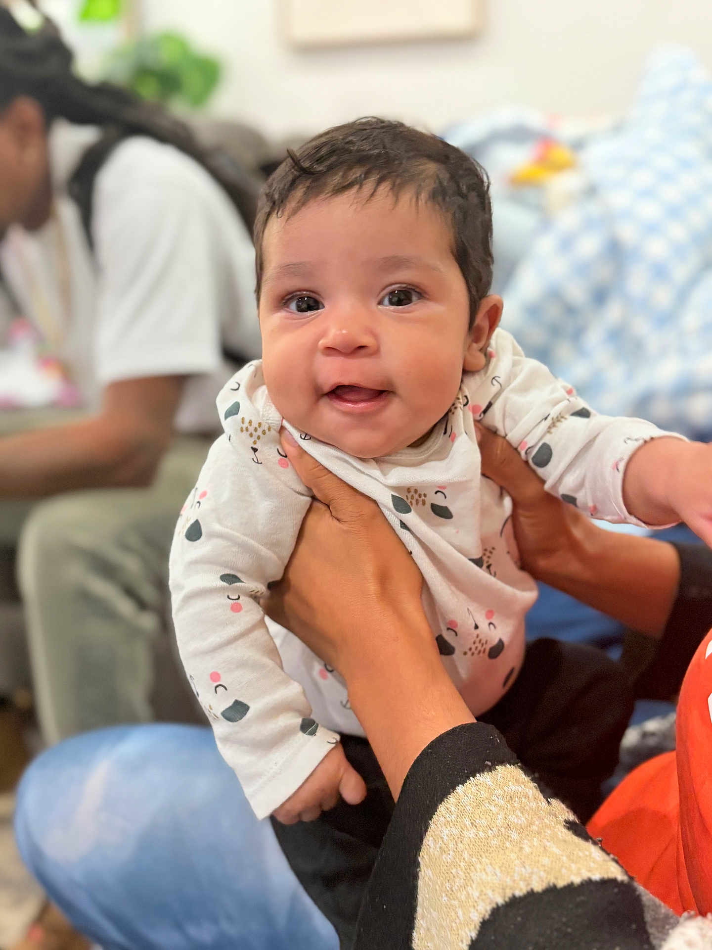 Twyla is registered to the contest to win money with this photo: baby, child, smiling, person, hands, clothing, patterned_outfit, indoor, blurred_background, cushion, seated_person, happy, cute, infant, portrait, closeup, skin, holding, face, eyes