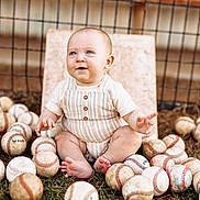Eastyn is registered to the contest to win money with this photo: baby, child, baseball, sports, outdoor, grass, fence, sitting, happy, blue_eyes, cute, playful, summer, clothing, barefoot, portrait, infant, toy, fun, nature