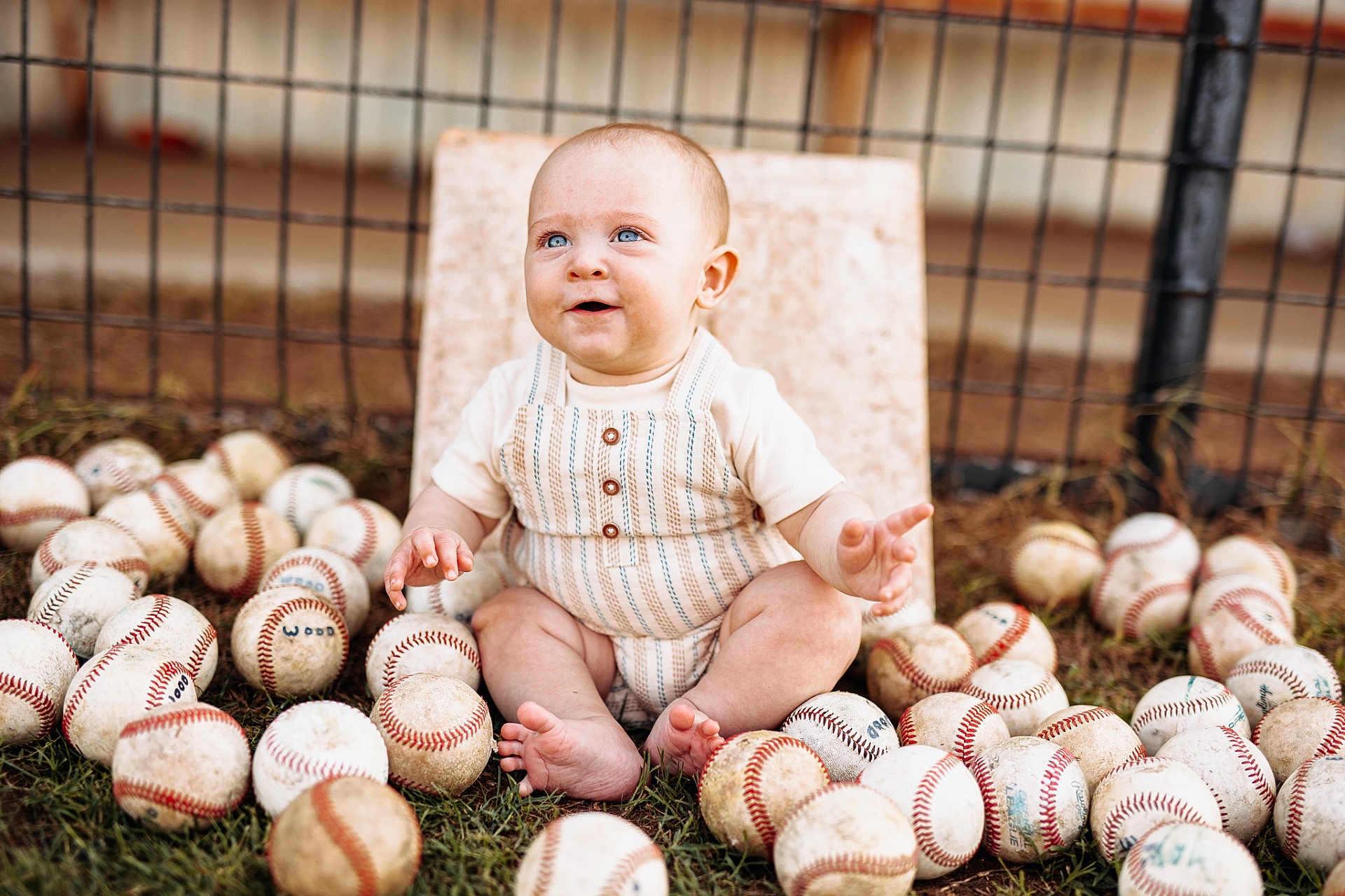 Eastyn is registered to the contest to win money with this photo: baby, child, baseball, sports, outdoor, grass, fence, sitting, happy, blue_eyes, cute, playful, summer, clothing, barefoot, portrait, infant, toy, fun, nature