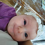 Daenerys participe au concours pour gagner de l'argent avec cette photo : baby, infant, child, face, eyes, headband, flower_headband, purple_shirt, closeup, portrait, lying_down, cheek, nose, mouth, skin, adorable, cute, blanket, patterned_background, fabric