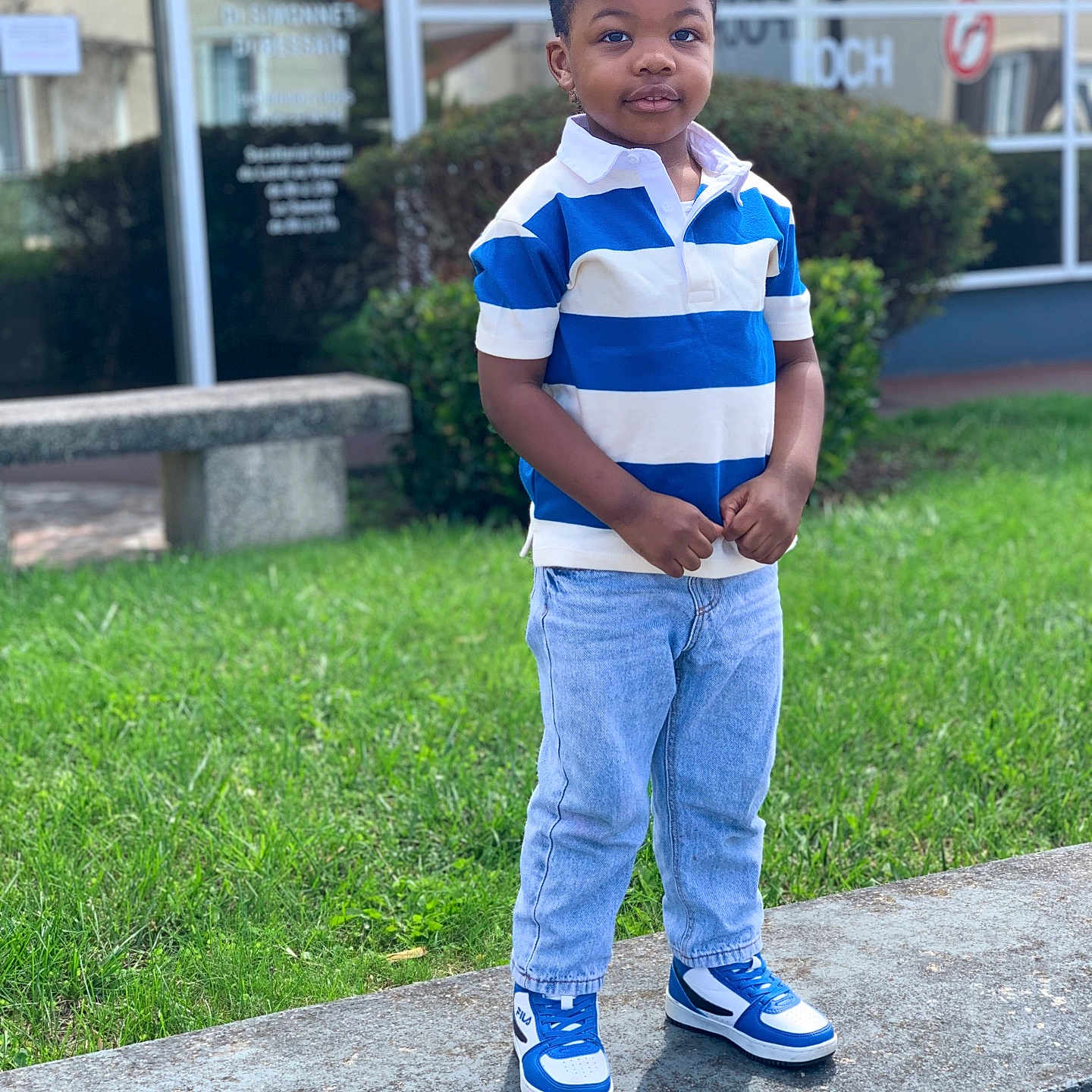 Enzo-Ebuwa Omosumwen a rejoint le concours — aidez-le/la à gagner de superbes lots ! bench, blue, boy, building, casual_clothing, child, cute, fashion, grass, greenery, jeans, outdoor, polo_shirt, portrait, smiling, sneakers, standing, urban, white, window