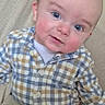 Emerson is registered to the contest to win money with this photo: baby, infant, child, portrait, sitting, blue_eyes, smiling, plaid_shirt, checkered_clothing, buttoned_shirt, beige_pants, cushion, indoor, close_up, face, head, eyes, fair_hair, happy, photography