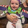 Emerson is registered to the contest to win money with this photo: baby, child, toddler, smiling, happy, portrait, costume, space_ranger, buzz_lightyear, purple_hat, green_suit, sitting, held, adult, family, indoors, toy_story, colorful, photobomb, closeup