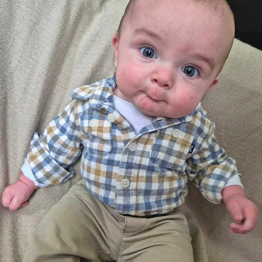 Emerson is registered to the contest to win money with this photo: baby, child, infant, portrait, sitting, armchair, couch, indoor, clothing, plaid_shirt, beige_pants, blue, wide_eyes, facial_expression, head, hands, legs, cozy, photography, smiling