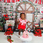 Averiana is registered to the contest to win money with this photo: toddler, child, birthday_cake, cake_stand, red_roses, strawberries, flower_garland, decorations, party, celebration, pink_dress, white_sandals, wooden_background, green_leaves, sign, flowers, standing, indoors, happy, festive