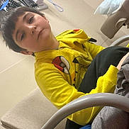 Luke joined the competition — help win amazing prizes! child, boy, yellow_hoodie, pikachu, indoor, chair, casual, relaxed, seated, short_hair, face, expression, person, clothing, furniture, background, office, technology, young, portrait