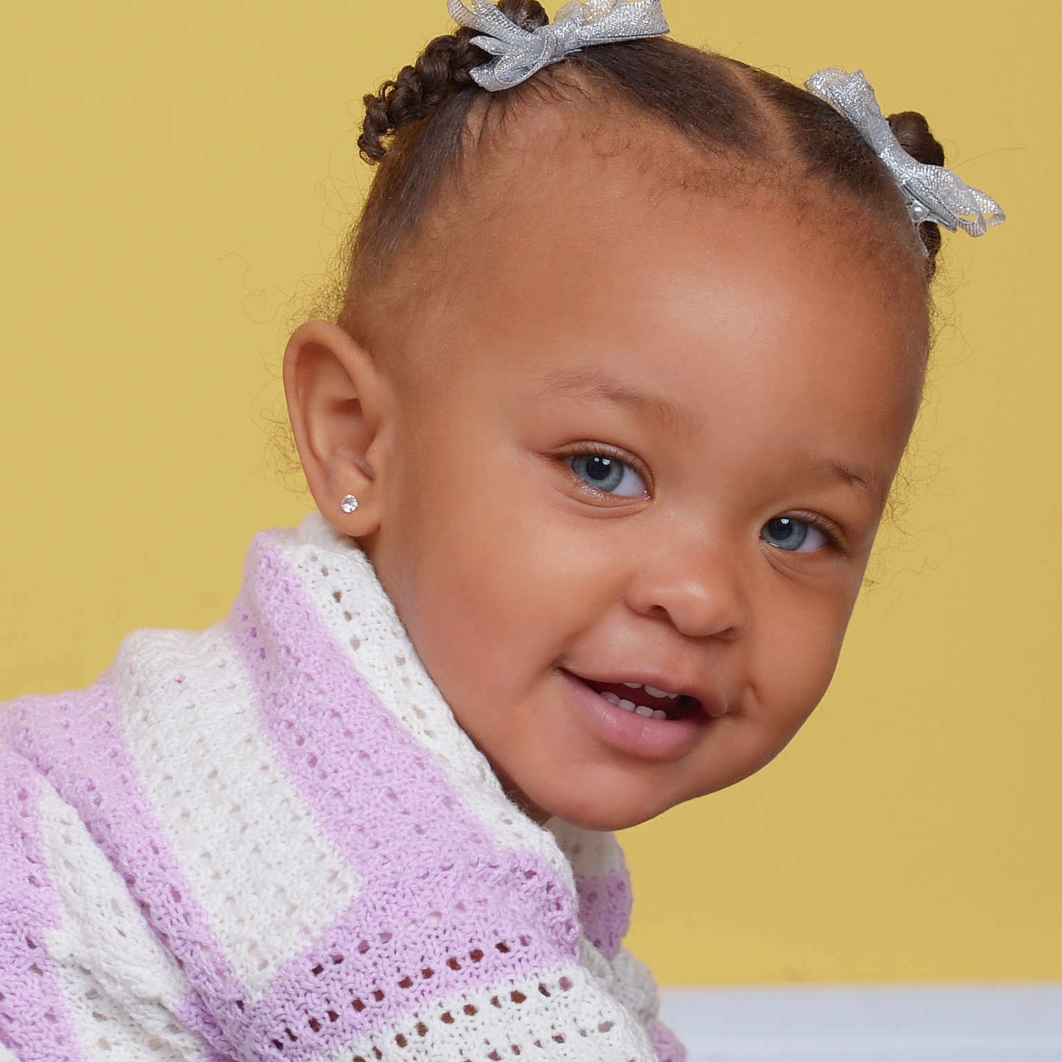 Bria is registered to the contest to win money with this photo: baby, blue_eyes, braided_hair, child, closeup, cute, earrings, face, fashion, happy, indoor, knitwear, person, portrait, purple_sweater, silver_bows, smile, toddler, white_sweater, yellow_background