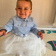 Maddy a rejoint le concours — aidez-le/la à gagner de superbes lots ! baby, child, smiling, blue_jacket, white_skirt, sitting, indoor, play_mat, cute, happy, person, young_child, toddler, clothing, floor, head_hair, face, funny_hair, portrait, adorable