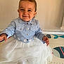 baby, child, smiling, blue_jacket, white_skirt, sitting, indoor, play_mat, cute, happy, person, young_child, toddler, clothing, floor, head_hair, face, funny_hair, portrait, adorable