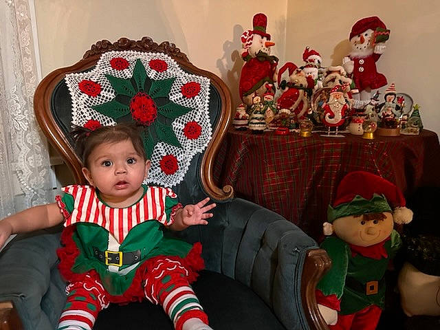 Joselyn joined the competition — help win amazing prizes! baby, baby_toddler_clothing, chair, christmas, christmas_decoration, christmas_eve, costume_hat, event, fictional_character, hat, headgear, holiday, human_body, lap, person, red, room, santa_claus, toddler, toy