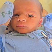 Raylan is registered to the contest to win money with this photo: baby, blanket, blue_clothing, child, close_up, curious_expression, cute, dinosaur_print, eyes, face, hand_near_head, head, indoors, infant, lying_down, newborn, onesie, portrait, skin, soft_lighting