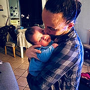 Thyago a rejoint le concours — aidez-le/la à gagner de superbes lots ! baby, adult, indoor, hug, kiss, love, affection, person, plaid_shirt, blue_clothing, tiled_floor, chair, table, curtain, lamp, hair_bun, home, cozy, family, parent