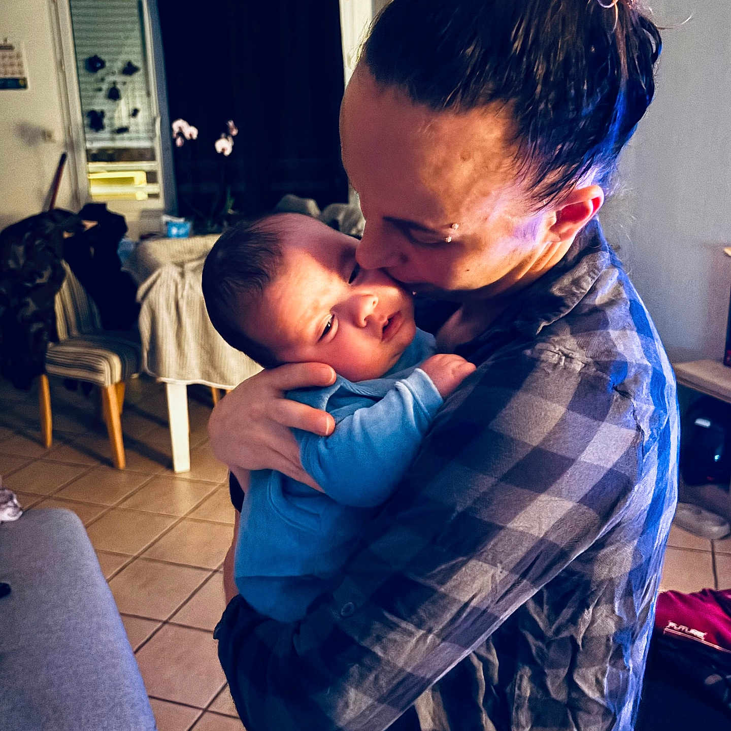 Thyago a rejoint le concours — aidez-le/la à gagner de superbes lots ! adult, affection, baby, blue_clothing, chair, cozy, curtain, family, hair_bun, home, hug, indoor, kiss, lamp, love, parent, person, plaid_shirt, table, tiled_floor
