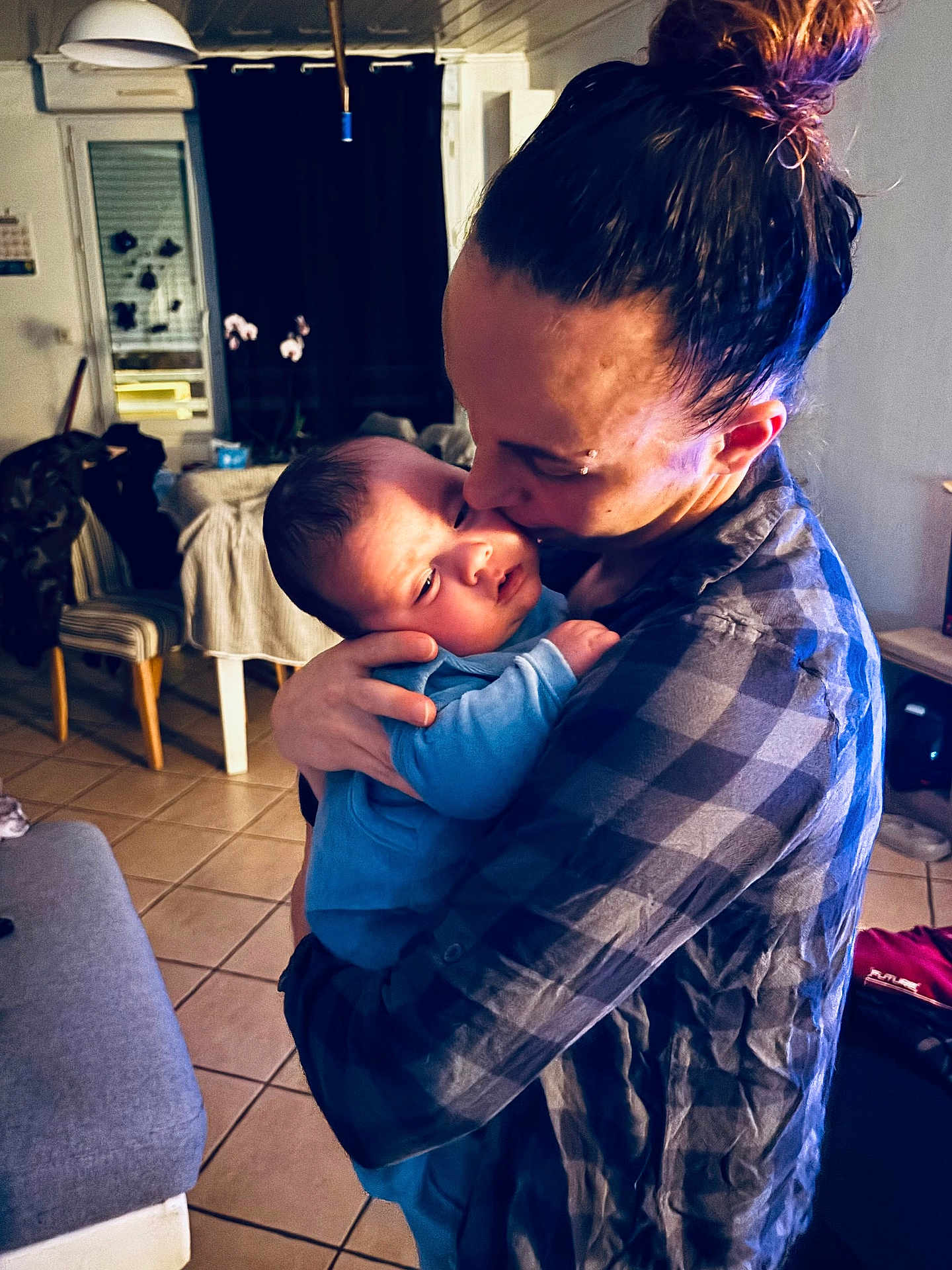 Thyago a rejoint le concours — aidez-le/la à gagner de superbes lots ! baby, adult, indoor, hug, kiss, love, affection, person, plaid_shirt, blue_clothing, tiled_floor, chair, table, curtain, lamp, hair_bun, home, cozy, family, parent