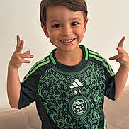 Saïd a rejoint le concours — aidez-le/la à gagner de superbes lots ! background, boy, casual, child, couch, cute, expression, face, gesture, green_jersey, hands, happy, home, indoor, person, portrait, short_hair, smiling, sportswear, young