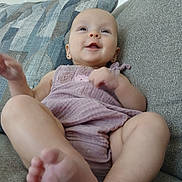 Athena is registered to the contest to win money with this photo: baby, smiling, couch, pillow, purple_outfit, happy, infant, face, arm, leg, foot, earrings, skin, indoors, child, relaxed, cute, comfort, portrait, seated