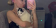 Luna a rejoint le concours — aidez-le/la à gagner de superbes lots ! woman, cat, mirror, selfie, headband, vanity_lights, bottle, countertop, scissors, black_and_white_cat, pink_headband, reflection, indoor, casual, young_adult, holding, phone, furniture, beauty_products, chair