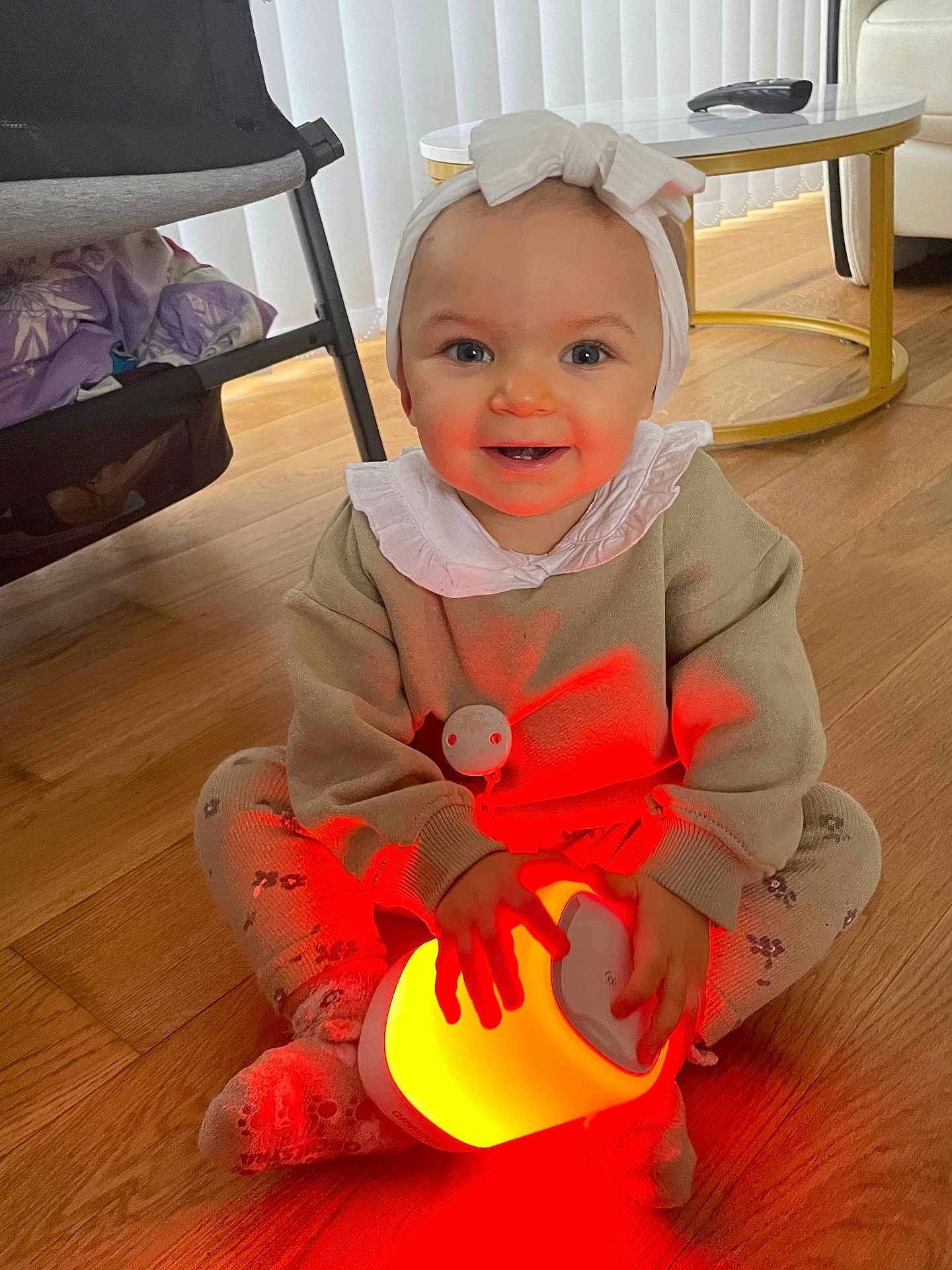 Loudjayne participe au concours pour gagner de l'argent avec cette photo : baby, child, glowing_lamp, headband, bow, smiling, sitting, floor, wooden_floor, leggings, patterned_clothing, cozy, indoors, table, remote_control, furniture, happy, cute, hands, face