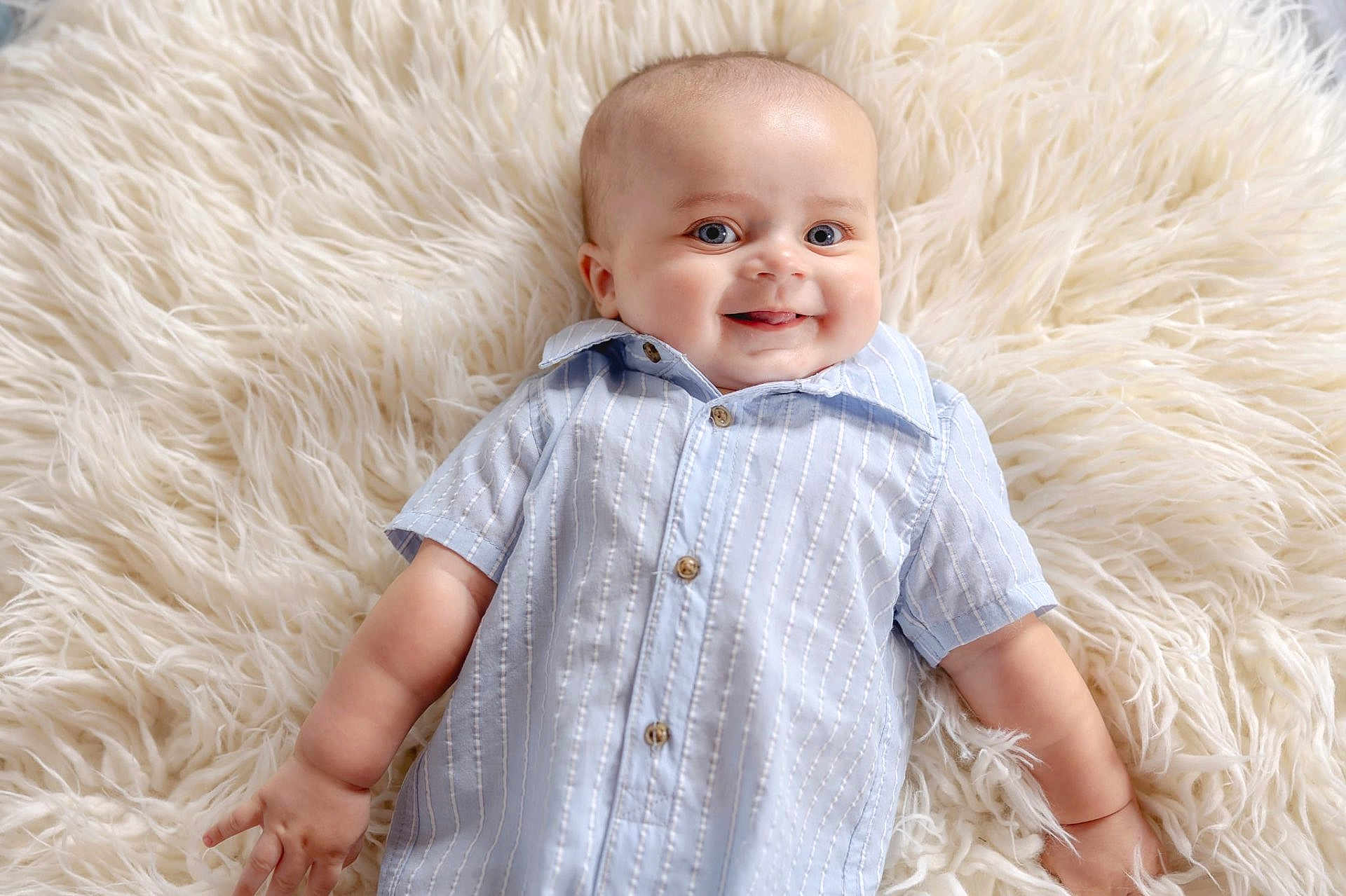 Amias is registered to the contest to win money with this photo: baby, infant, smiling, blue_eyes, shirt, striped_clothing, fluffy_rug, soft_texture, happy, cute, child, portrait, lying_down, skin, cheeks, hand, fingers, light, indoors, cozy