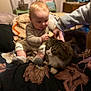 baby, cat, hand, bed, blanket, indoor, person, child, furniture, animal, cozy, curious, tabby_cat, soft_lighting, warm_colors, interaction, caring, human_animal_bond, cute, relaxed