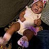 baby, infant, child, portrait, smiling, curious, sitting, lying_down, indoors, couch, blanket, headband, bow, floral_pattern, strawberry, romper, socks, dark_background, home, face