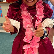 Egypt is registered to the contest to win money with this photo: accessories, bookshelf, carpet, child, classroom, costume, dress_up, happy, indoor, maroon_dress, person, pink_flower_lei, playful, portrait, red_hat, smiling, sunglasses, thumbs_up, toy, white_ruffles