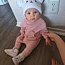 Lietys is registered to the contest to win money with this photo: baby, child, pink_outfit, bear_design, white_hat, hat_with_ears, sitting, wooden_floor, hand_holding, curious_expression, indoor, footwear, sneakers, cute, person, infant, wall_outlet, light_skin, flooring, portrait