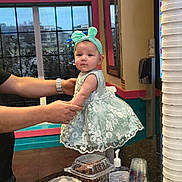 Lietys is registered to the contest to win money with this photo: baby, child, person, dress, headband, hands, counter, cup, food_container, window, indoor, table, clothing, decor, adult, wall, mirror, bracelet, hand_sanitizer, plastic_cup
