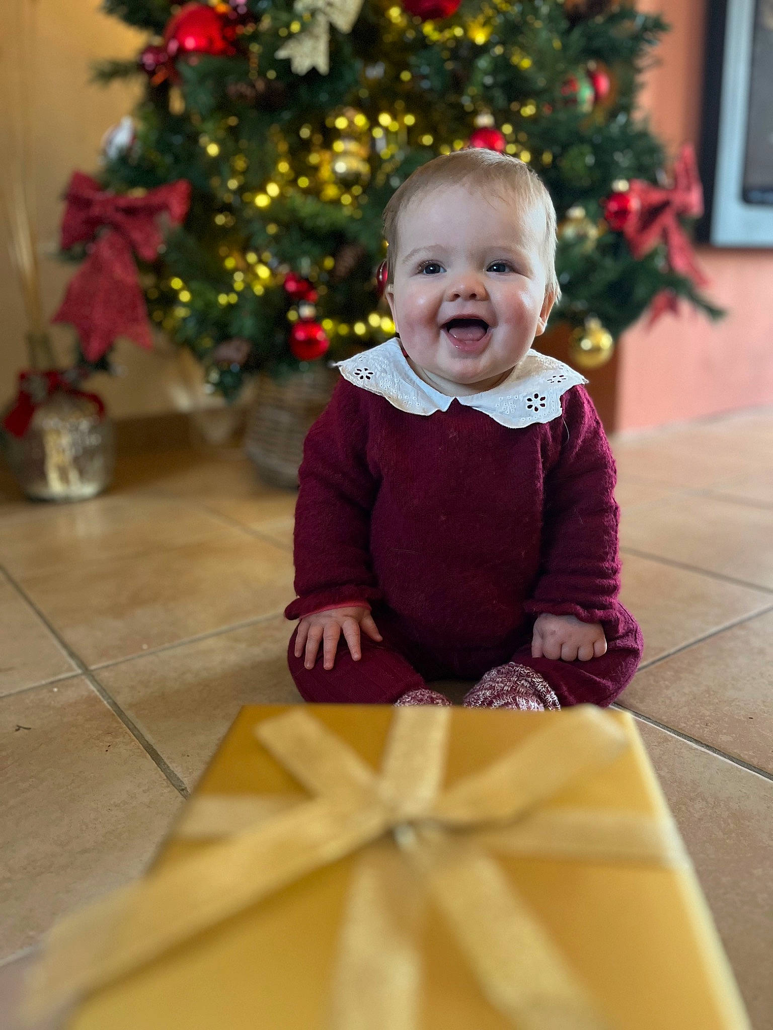 Lalie participe au concours pour gagner de l'argent avec cette photo : baby, baby_toddler_clothing, christmas_decoration, christmas_ornament, christmas_tree, dress, face, facial_expression, flooring, fun, happy, jacket, person, plant, sleeve, smile, standing, toddler, tree, white