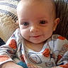 Braxton is registered to the contest to win money with this photo: baby, child, infant, smiling, portrait, sitting, indoors, couch, blanket, clothing, onesie, sports_pattern, basketball, football, face, eyes, hands, happy, home, close_up