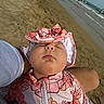 baby, infant, sleeping, beach, sand, ocean, waves, sun_hat, pink_outfit, floral_pattern, outdoor, portrait, face, closed_eyes, peaceful, adult_arm, held_baby, shoreline, summer, relaxing