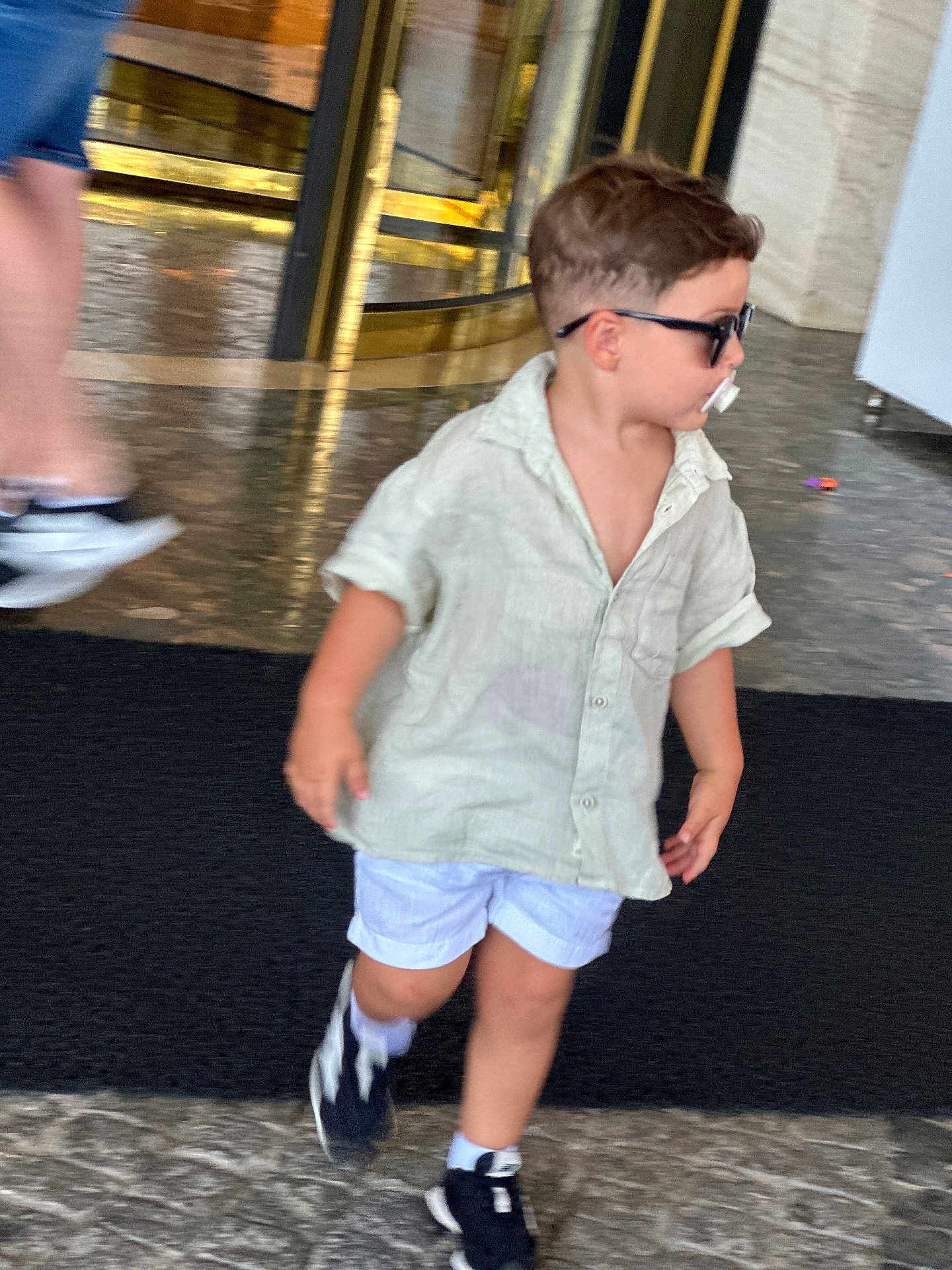 Matteo participe au concours pour gagner de l'argent avec cette photo : toddler, child, sunglasses, pacifier, shorts, shirt, sneakers, walking, indoor, floor, marble, person, motion_blur, fashion, casual, young_child, cute, hair, legs, adult