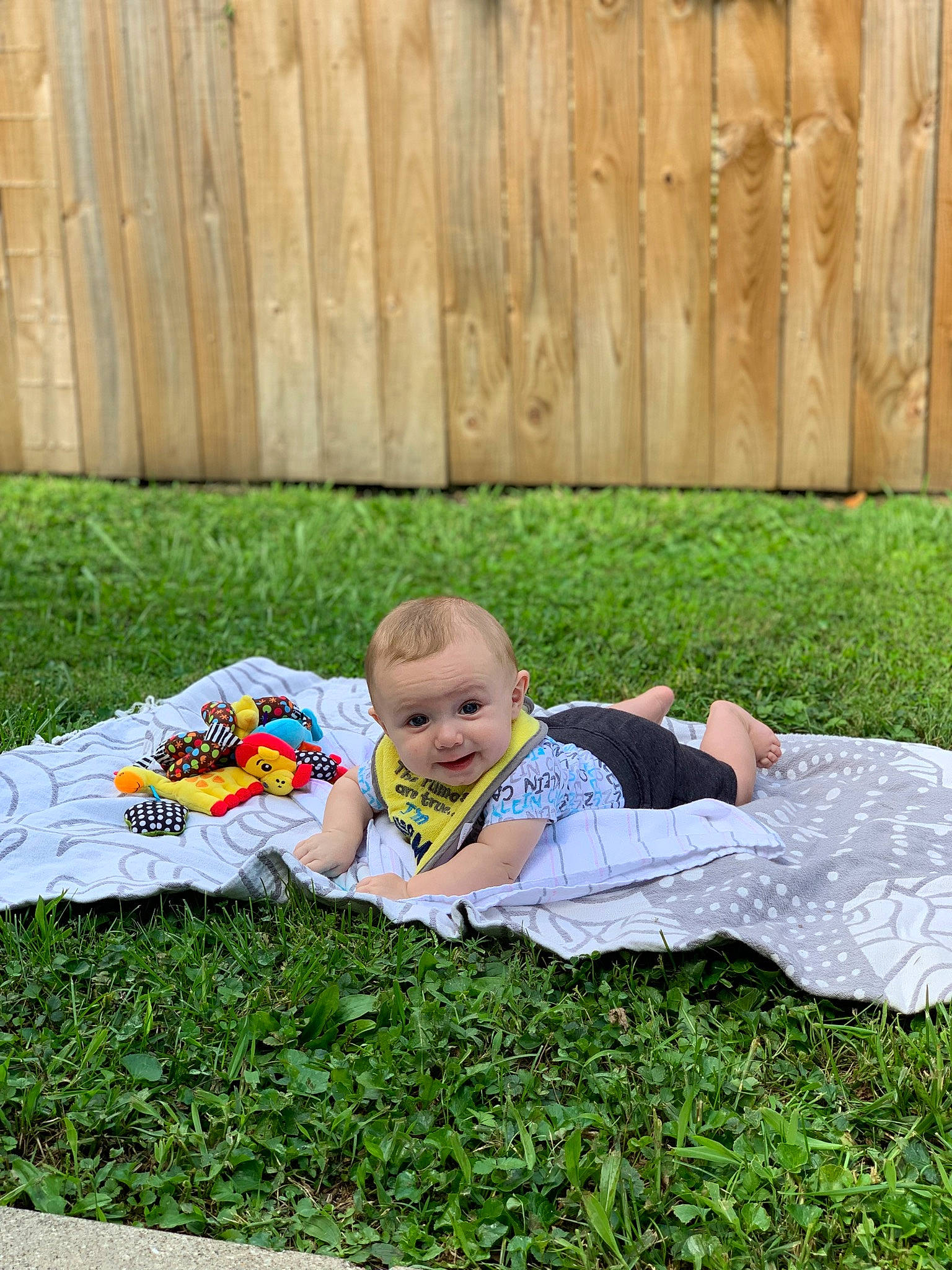 Alaric is registered to the contest to win money with this photo: baby, baby_toddler_clothing, fence, fun, grass, grassland, groundcover, happy, landscape, lawn, leisure, meadow, people_in_nature, person, plant, recreation, sitting, smile, t_shirt, toddler