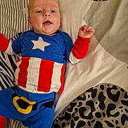 Christopher joined the competition — help win amazing prizes! baby, child, costume, captain_america, blue_clothing, red_clothing, white_star, bedspread, patterned_bedspread, face, head, lying_down, infant, one_arm_raised, cute, indoor, person, smiling, young_child, superhero_outfit