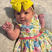 Kinsley is registered to the contest to win money with this photo: baby, child, headband, yellow_bow, dress, floral_pattern, colorful_clothing, blanket, fist, cute, infant, portrait, soft_texture, laying_down, indoors, person, skin, face, expression, small