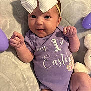 Kinsley joined the competition — help win amazing prizes! baby, infant, headband, bow, purple_onesie, text_on_clothing, easter, blanket, plush_toy, easter_eggs, soft_texture, cute, smiling, lying_down, indoors, child, person, portrait, celebration, holiday