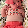 baby, baby_girl, child, closeup, clothing, cute, floral_cushion, headwear, indoors, infant, pattern, person, pink_bow, pink_shorts, playful, relaxed, smiling, strawberry_shirt, tongue_out, young
